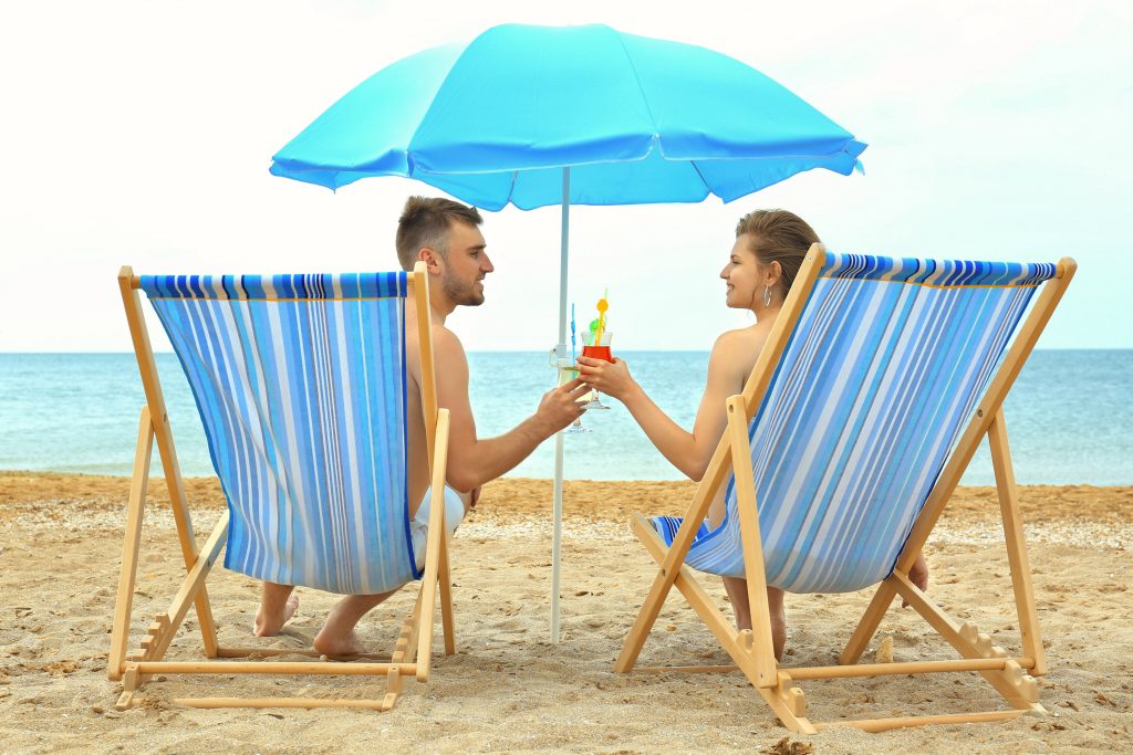 Young couple with cocktails sitting on beach chairs at sea shore